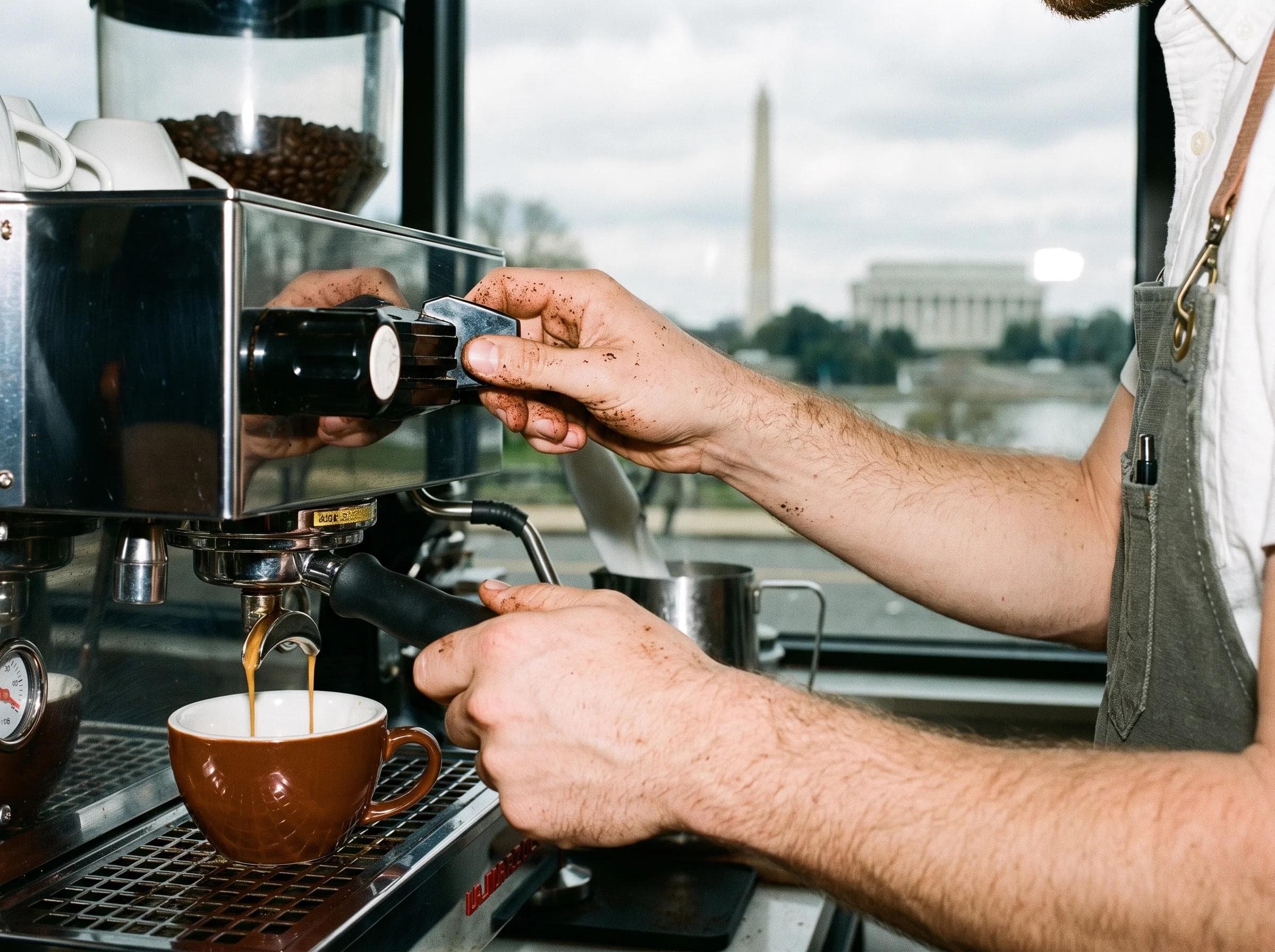 Close-up of a barista preparing an espresso drink with DC monument architecture softly visible in the background